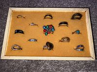 Top-down photo showing all 15 rings arranged on a yellow felt-lined ring holder case with cream-colored edges.