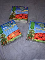 Three boxed Topsy Turvy tomato planters placed on fabric surface, showing front of boxes with product branding and images.