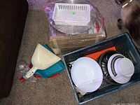 Photo showing plastic drying racks, a basket, and dust pans on the floor near a plastic crate.