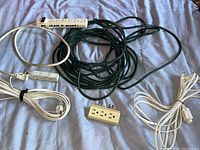 Photo showing all three extension cords and three white six-outlet power strips together on a surface.