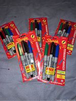 Photo showing six unopened packs of Sharpie permanent markers in various colors including red, blue, green, and black, each with a bonus free marker included.