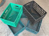Five plastic crates in teal and black stacked and arranged on a concrete and stone surface.