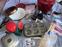 Photo showing assortment of kitchen appliances and utensils including mini waffle maker, frying pans, chopper, muffin pan, spatula, and more.