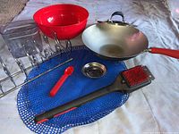 Overview of kitchen items including walk pan with lid, mixing bowls, plate holder, nonslip mat, grill brush, metal scrubber, and plastic spoon/fork stack