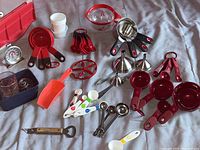 Top-down view showing red nesting measuring cups, colored measuring spoons, stainless funnels, a red scoop, egg slicer, and other kitchen tools arranged on a surface.