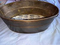 Side angled view of oval vintage metal bucket showing oval shape, ribbed detailing, and handle on side.