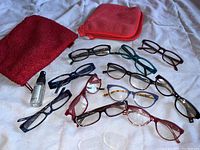 Overview of multiple pairs of women's prescription glasses in varied frame styles and colors, along with cleaning cloths and bag.