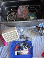 Photo showing a large black storage container filled with various tools and organizers, several small compartments, a pink thermos bottle, a white light bulb, and assorted hardware.
