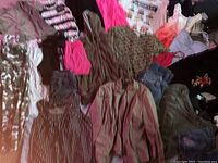 View of assorted women's clothing including patterned blouses, pink tank tops, graphic T-shirts, and trousers spread on the floor.