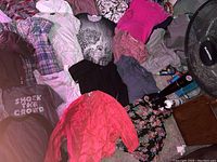 Display of various women's clothing items including T-shirts, long sleeve shirts, blouses, and dresses arranged on floor