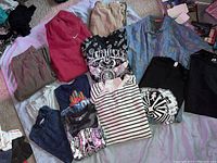 Overview of men's clothing laid out including jeans, sweatpants, various T-shirts and shirts on a light purple surface