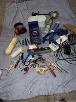 Wide view of tools, gloves, rollers, clamps, wire brush, electrical cords, squeegees, and cans on blue cloth.