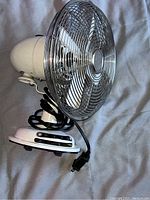Side angle view of the vintage white electric fan showing chrome blade guard, white body, and black power cord.