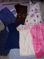 Seven women's dresses laid out on floor showing various colors and patterns, medium and large sizes.