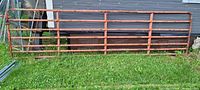 Full view of 16-foot orange tubular livestock gate leaning against building