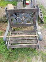 Front view of garden bench showing decorative cast iron end with dragonfly and leaves and wooden slats seat with visible damage.