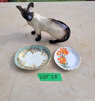 Full view of Beswick Siamese cat figurine with two decorative dishes on a beige surface, labeled Lot 28.