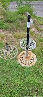 Three cast iron umbrella stands placed on grass showing overall condition and size.