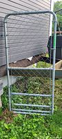 Full view of the rectangular chainlink gate with tubular metal frame and diamond mesh, placed outdoors on grass near a building.