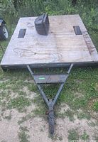 Front angled view showing plywood deck with cutouts for wheels, triangular metal frame and hitch in grass.