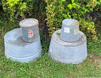 Four galvanized metal containers displayed outdoors on grass and surrounded by greenery, showing their size, condition and surface textures.