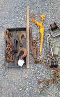 Overview of all items including chains, hooks, load binder, turnbuckles, and pulleys arranged on gravel surface.