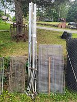View of multiple vertical metal uprights with attached mounting brackets, and several chrome wire shelves of varying widths arranged outdoors on grass.
