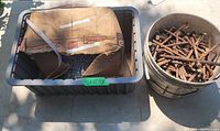 Plastic bin with a cardboard box inside holding small 1 inch Ardox nails on the left, and a pail filled with larger rusty 6 inch common nails on the right.