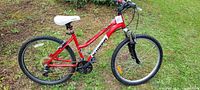 Red Schwinn mountain bike on grass showing full side view including frame, tires, seat, and handlebars.