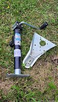 Full view of black 5000 lb trailer jack with crank handle lying on grass next to a silver mounting bracket.