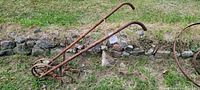 Side view of two rusty vintage walking cultivators on grass near stone wall