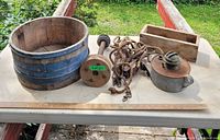 Wide photo showing the wooden bucket, pulley, coil of rope, wooden box, and metal lamp arranged on a white tabletop outdoors.
