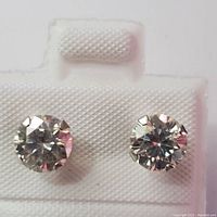 Front view of two round faceted moissanite studs on white earring card