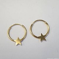 Front view of two 14K yellow gold hoop earrings each featuring a five-point solid star charm on a white background.