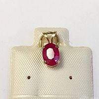 Front view of the 14K yellow gold pendant with oval ruby in four-prong setting on a textured display card.