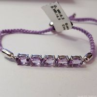 Close-up view of the five rectangular faceted amethyst stones set in silver-tone metal on a braided purple cord band.