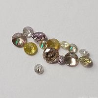 Loose diamonds and colored gemstones scattered on white background, showing a variety of cuts and colors.