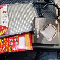 View of Instant TAC adhesive sheets in retail packaging alongside a compact LED light panel and Solar Showcase BD display stand in box with attached lamp.
