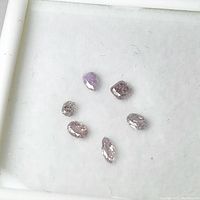 Six assorted natural pink diamonds displayed loose on white background. Various diamond shapes visible: cushion, oval, pear, marquise, round cuts.