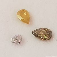 Three pear-shaped faceted gemstones on white background, one pink diamond (~0.5ct), one yellow-orange, one brownish gemstone.