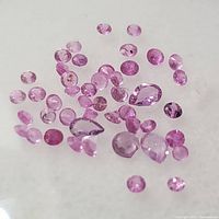 Close-up top view of numerous small pink faceted sapphire stones spread on a flat surface
