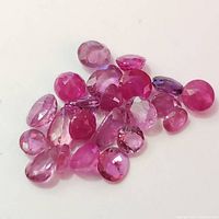 Close-up photo of multiple small, faceted loose rubies in red to pink hues on a white background.