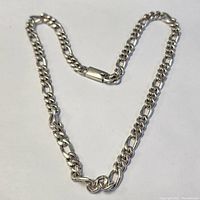 Full length view of silver chain necklace laid flat in a loose heart shape showing its curb link design and clasp.