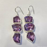 Top-down view of the pair of silver-framed amethyst earrings showing the three faceted stones per earring with deep purple color variations.