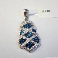 Silver pendant featuring multiple oval blue topaz stones set with crisscrossing bands studded with small white crystals, shown top-down view.