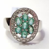 Close front view of silver ring with seven oval emerald stones clustered in the center, surrounded by textured silver border.