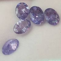 Close-up top view of five oval faceted tanzanite gemstones on a white surface.