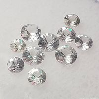 Close-up of ten loose white sapphire gemstones showing round brilliant cut and clear appearance on white background.