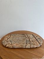 Brown marble oblong tray on wooden round table, top view showing natural marble veining and carved handles.