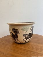 Side view of vintage planter pot showing black horse designs with green clouds on beige ceramic.
